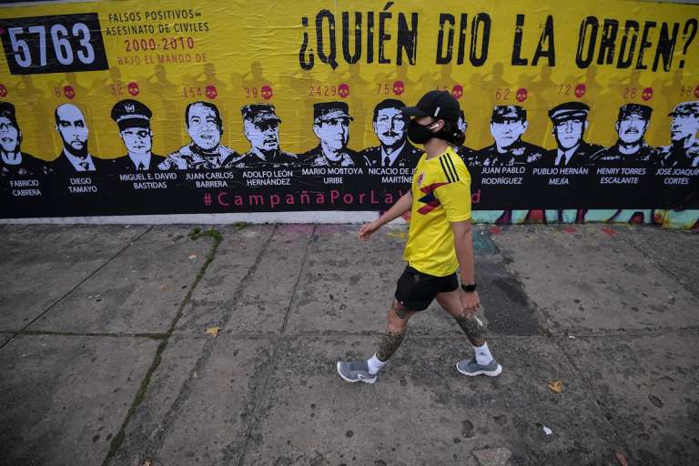 Hombre con la camiseta de Colombia camina frente al mural quien dio la orden donde están los rostros de militares investigados por falsos positivos.