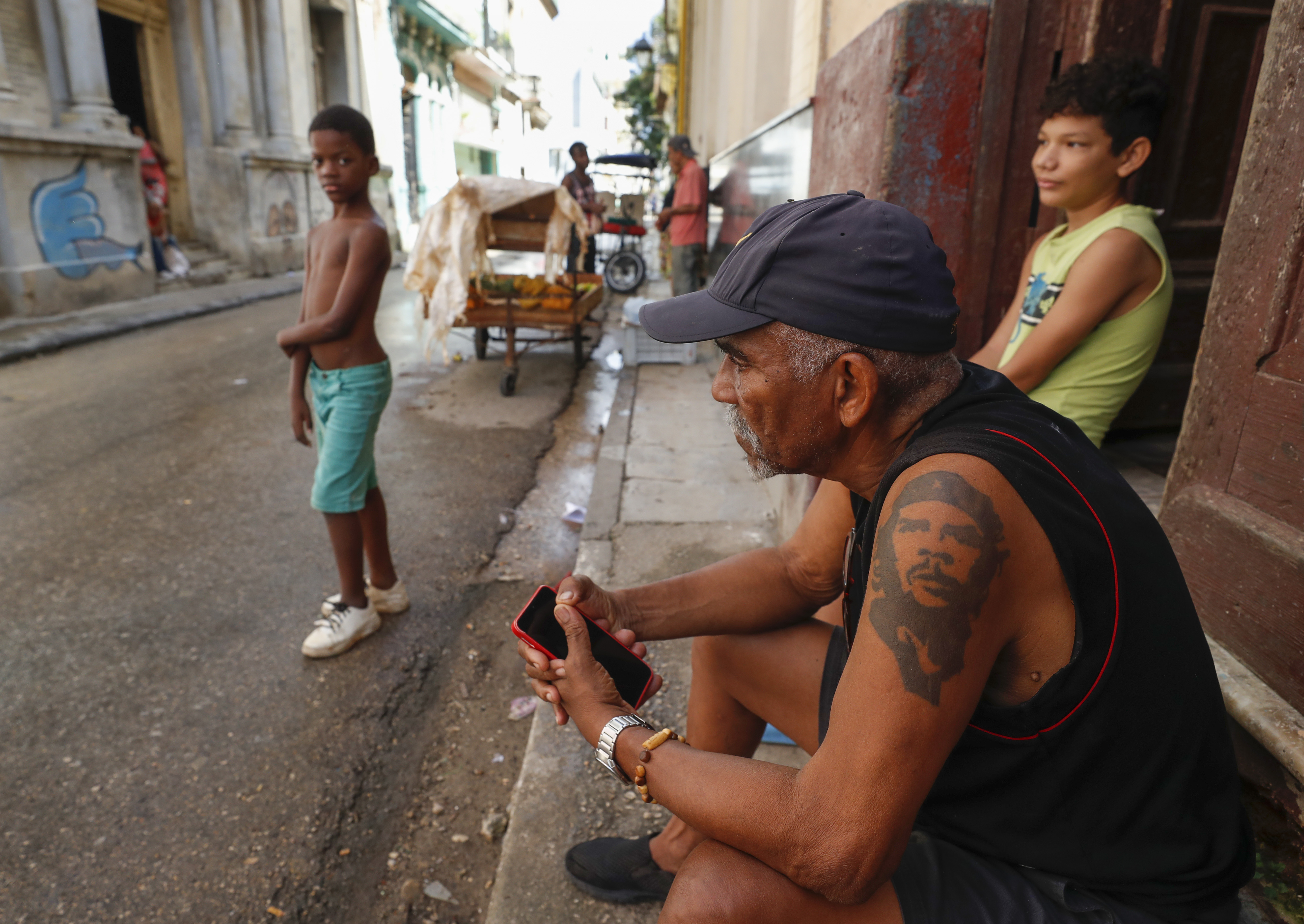 AME9446. LA HABANA (CUBA), 21/10/2024.- Un hombre con tatuaje del 'Che', espera sentado en la puerta de su casa a que llegue la corriente este lunes en La Habana (Cuba). El Gobierno cubano aseguró este lunes que "se ha ganado en fortaleza" en lo que va de día y avanzó que en las próximas horas se aumentará también la capacidad generación con la entrada de varias centrales termoeléctricas, revirtiendo gradualmente los efectos del apagón total del viernes. EFE/ Yander Zamora