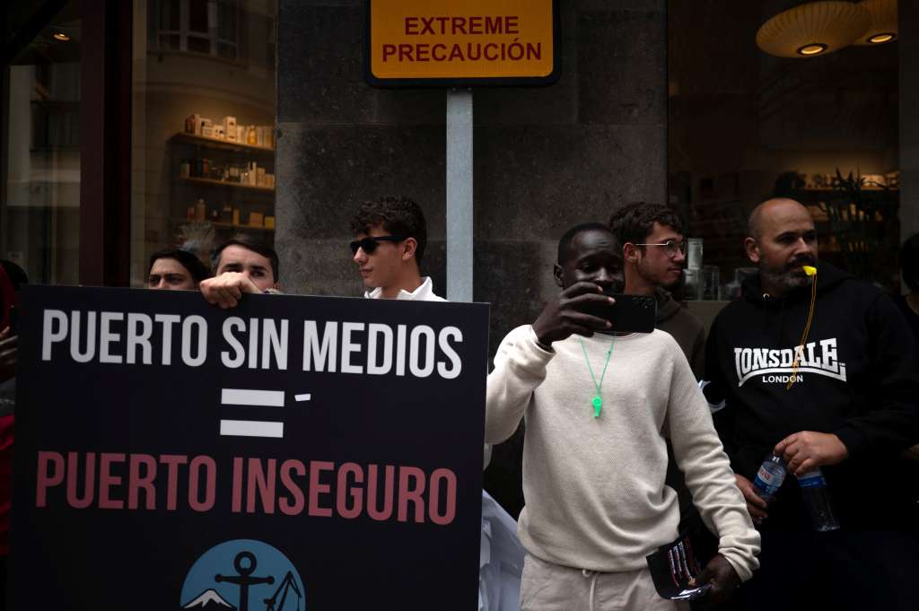 Dockers hold a banner reading 'Workers of Tenerife Port - TPT (Trabajadores del Puerto de Tenerife) - Port without means, Port unsafe' as they protest against the arrival of a cruise ship affected by hantavirus in Santa Cruz de Tenerife on May 8, 2026. Passengers aboard the MV Hondius cruise ship affected by a deadly hantavirus outbreak will start being flown to their countries of origin after the vessel arrives on the Canary island of Tenerife on May 10, 2026, the Spanish government said. (Photo by JORGE GUERRERO / AFP)