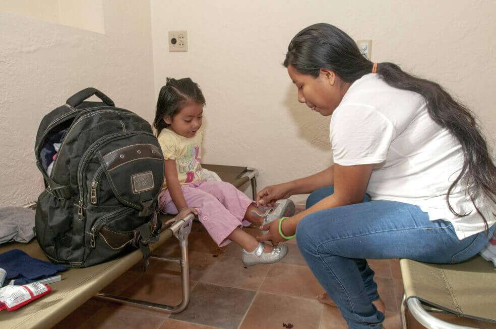 La guatemalteca Lidia Xol pone los zapatos a su hija Lea Che, de 4 años, en el interior del Monasterio Benedictino de la ciudad de Tucson en Arizona. / EFE