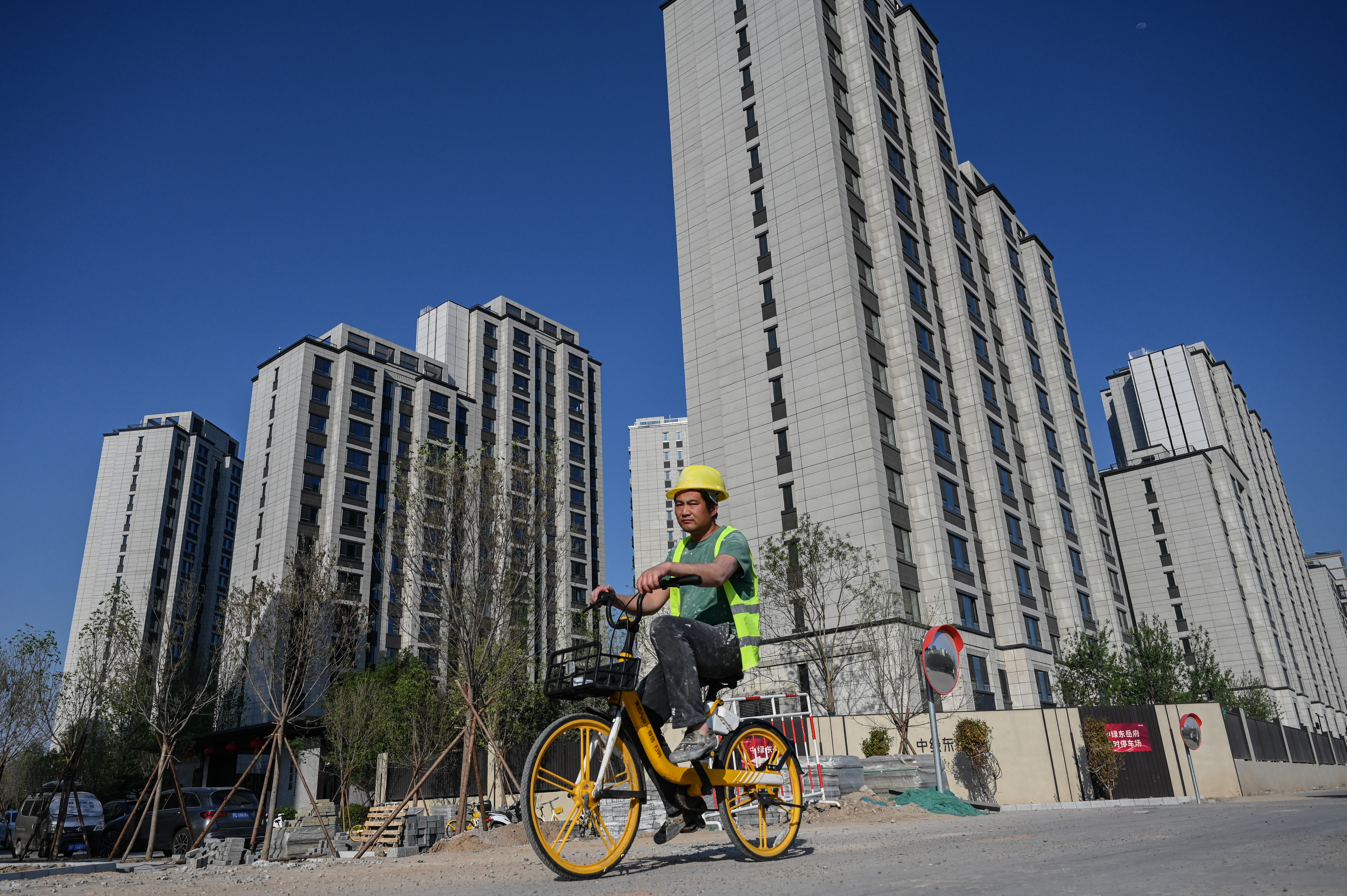 A worker rides a bicycle past a housing complex under construction in Beijing on May 17, 2024. (Photo by JADE GAO / AFP)