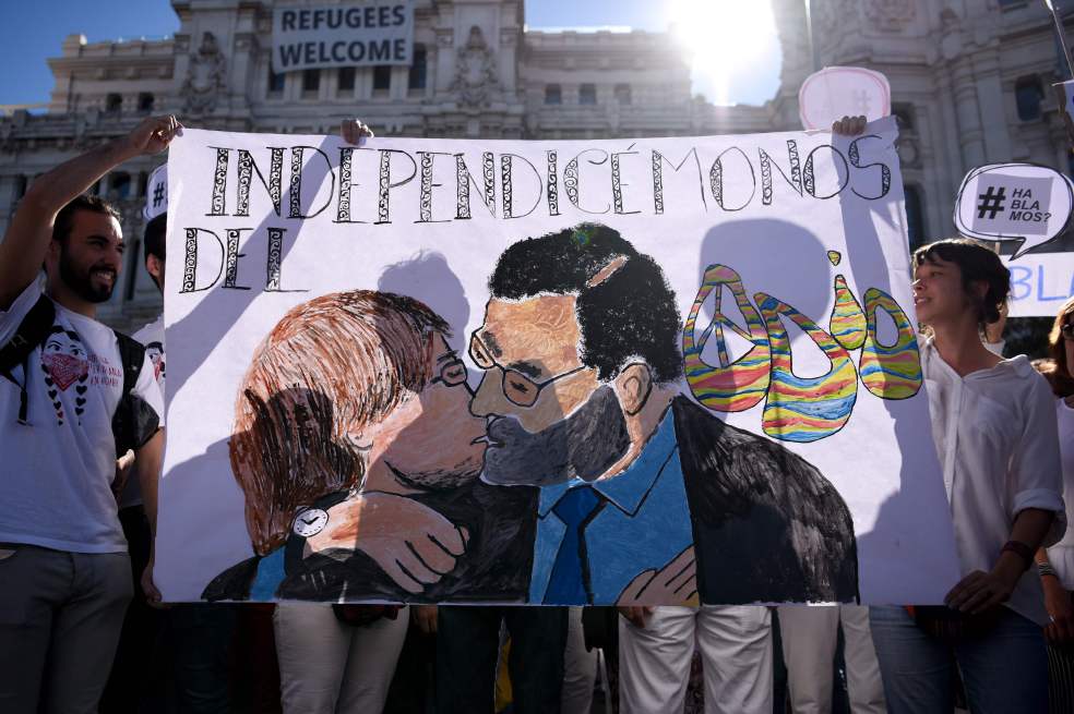 Manifestantes sostienen un cartel pintado en el que el presidente Mariano Rajoy besa al presidente catalán, Carles Puigdemont. / AFP
