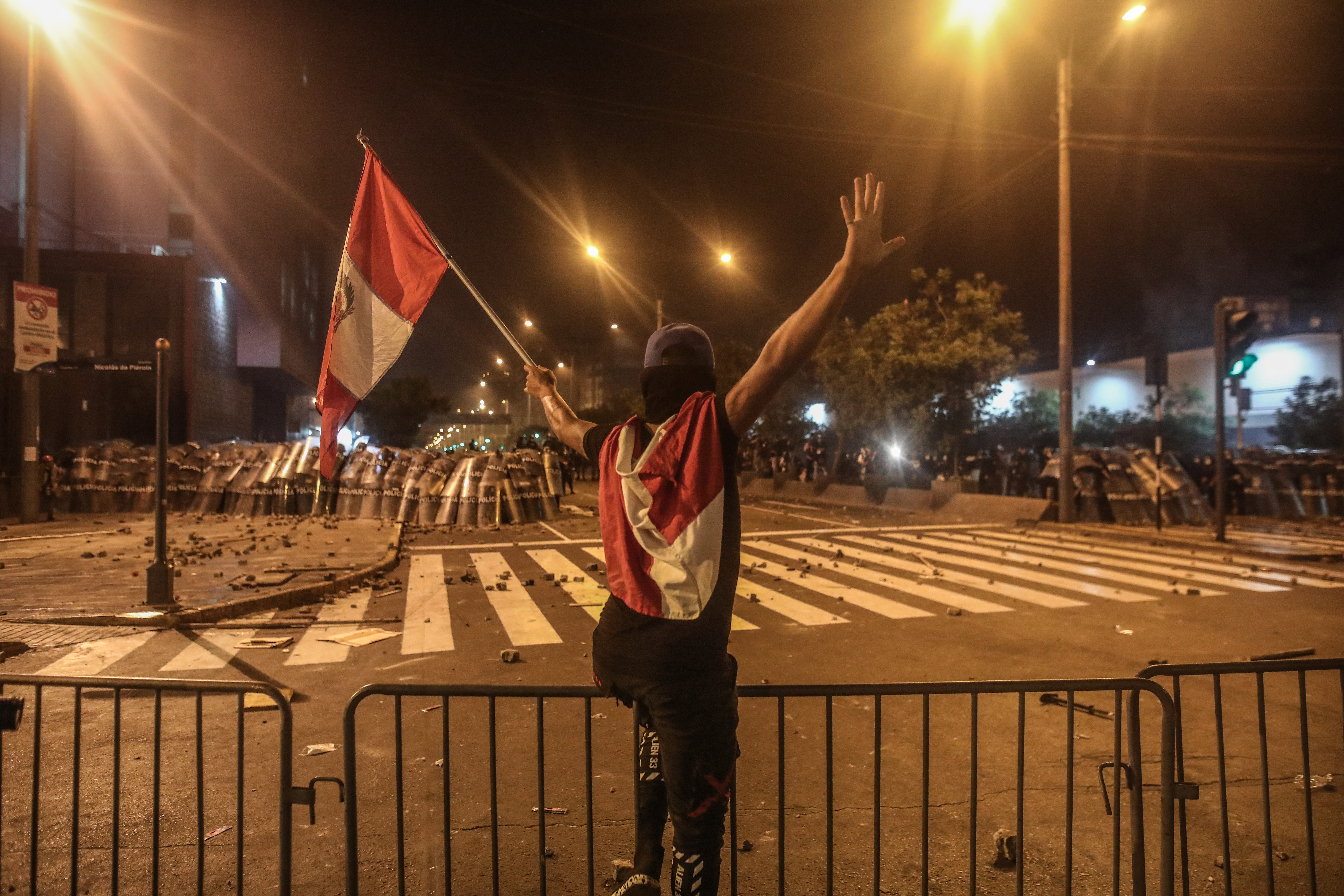 -FOTODELDÍA- AME9218. LIMA (PERÚ), 05/04/2022.- Un manifestante ondea una bandera frente a un cerco policial hoy, en Lima (Perú). Miles de peruanos desafiaron este martes el toque de queda ordenado por el presidente Pedro Castillo para Lima y su vecina provincia de Callao y se manifestaron en la capital para pedir la renuncia del mandatario. EFE/ Aldair Mejía