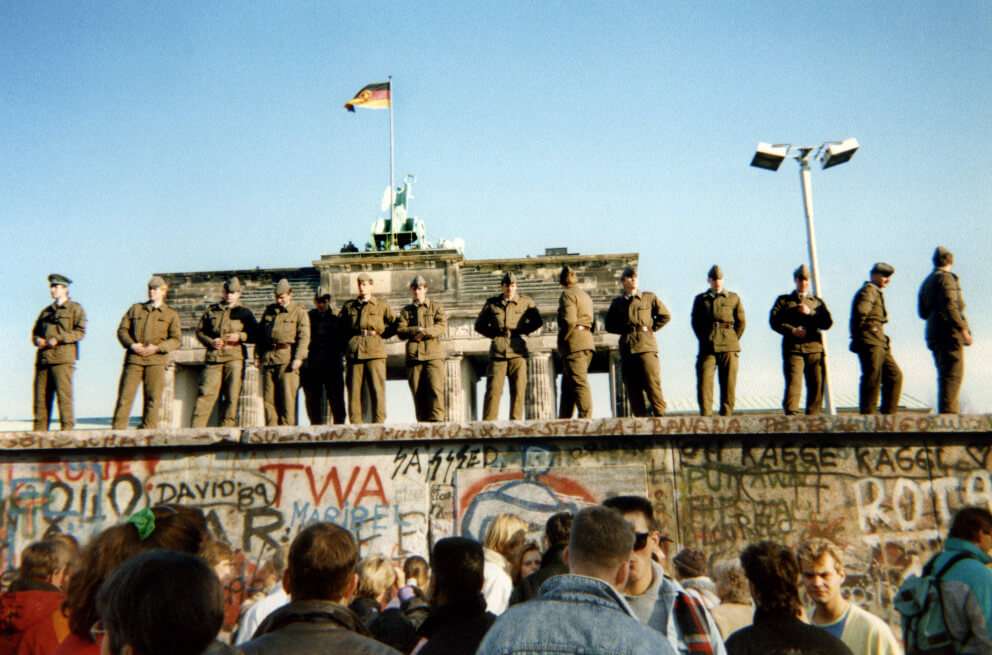 Si la democracia liberal va a sobrevivir y si vamos a derribar todos los muros (invisibles y literales) que hemos venido creando, es clave reconocer dónde se perdió el rumbo. / Foto: Guardias fronterizos de Alemania Oriental se paran en una sección del muro de Berlín con la puerta de Brandenburgo al fondo en Berlín, el 11 de noviembre de 1989. AFP