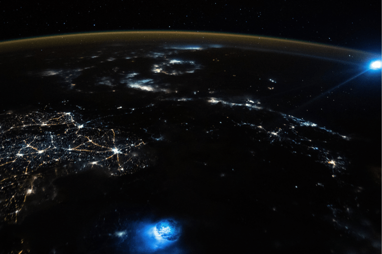 Un astronauta a bordo de la ISS tomó una imagen de la Tierra que contiene dos extrañas manchas azules de luz que brillan en la atmósfera de nuestro planeta. Curiosamente, las dos manchas no tienen ninguna relación entre sí y se han producido al mismo tiempo.
La primera mancha de luz, visible en la parte inferior de la imagen, es un enorme rayo que cayó junto a un gran hueco circular en la parte superior de las nubes.
La segunda mancha azul, que puede verse en la parte superior derecha de la imagen, es el resultado de la luz deformada procedente de la Luna.