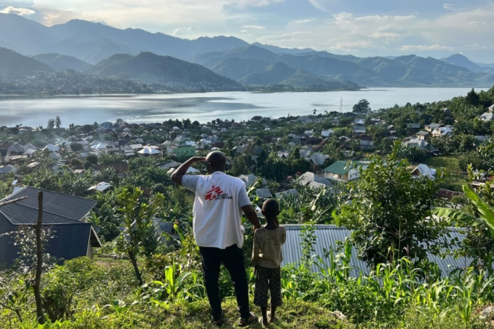 Un miembro de Médicos Sin Fronteras y un niño contemplan la ciudad de Minova y el lago Kivu desde lo alto de una colina en la provincia de Kivu del Sur, República Democrática del Congo.