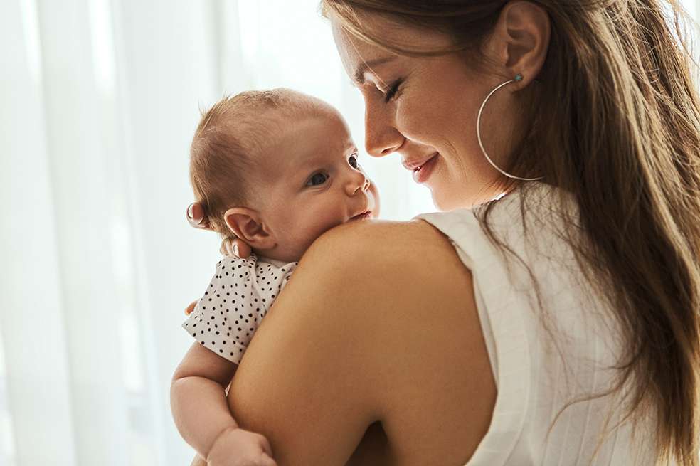 Beautiful mother kissing here little cute baby. Madre cargando a su bebé en casa