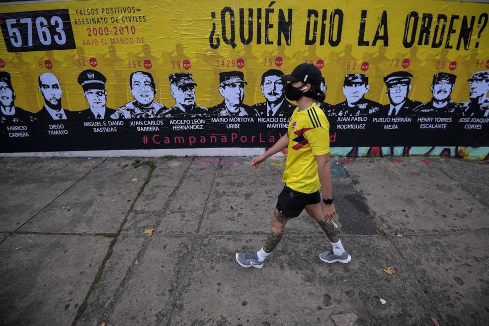 Hombre con la camiseta de Colombia camina frente al mural donde están retratados militares investigados por falsos positivos.