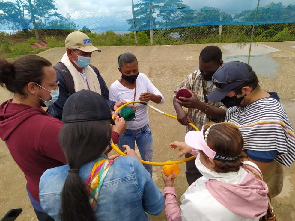 un grupo de personas realizan una actividad grupal: enrrollan hilo al rededor de un aro para hacer una mandala.