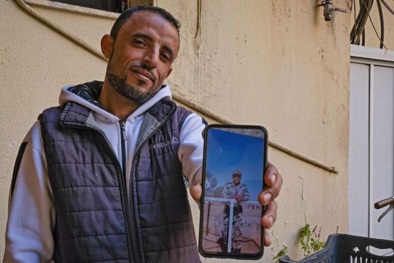 Fahad al-Routayban, un refugiado sirio de 30 años, posa para una foto del edificio donde trabaja como conserje, en la ciudad portuaria de Trípoli, en el norte de Líbano, mientras sostiene un teléfono que muestra una foto de él mismo hace 11 años como soldado del ejército sirio. Routayban huyó de su ciudad natal de Raqa al Líbano en 2013, por temor a que el ejército sirio lo llamara al servicio militar, lo que finalmente sucedió cuando sus padres recibieron una citación oficial en su nombre. Routabyan cambió de dirección al menos 10 veces mientras cruzaba el Líbano de sur a norte, hasta que finalmente se instaló en Trípoli, donde se casó.