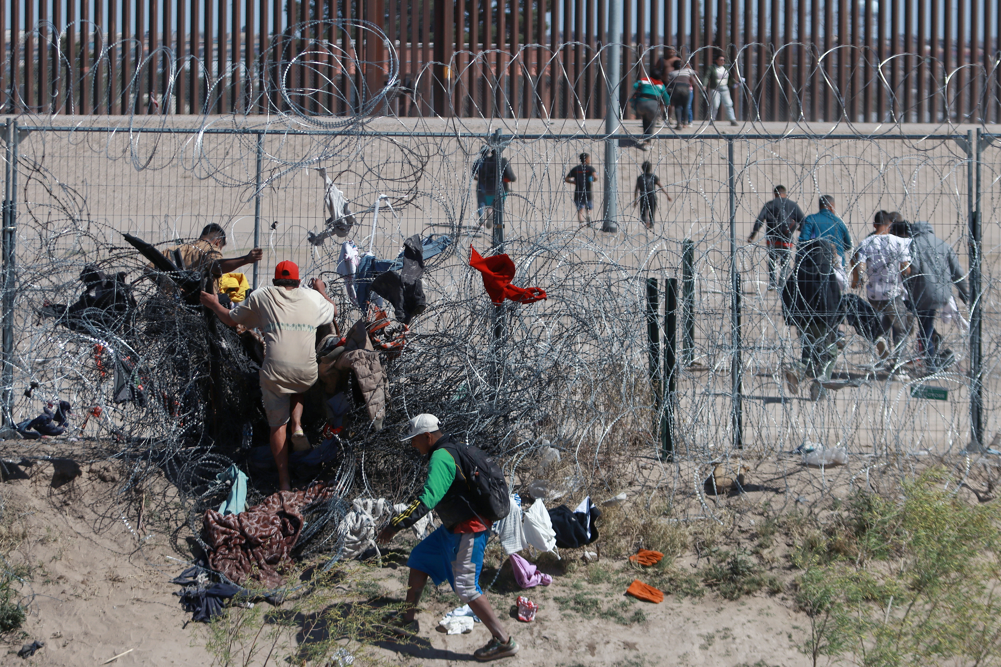 MEX2031. CIUDAD JUÁREZ (MÉXICO), 15/03/2024.- Migrantes cruzan una alambrada de navajas y púas, en la frontera que divide a México de los Estados Unidos, el 14 de marzo de 2024, en Ciudad Juárez (México). Los migrantes que cruzan la frontera afrontan nuevos riesgos porque Estados Unidos ha comenzado a descargar en el río Bravo el agua que le corresponde a México por tratado, por lo que quedan atrapados entre la corriente y el cerco de navajas que el Gobierno de Texas se niega a quitar. EFE/Luis Torres