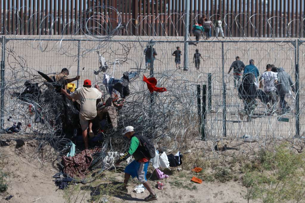 MEX2031. CIUDAD JUÁREZ (MÉXICO), 15/03/2024.- Migrantes cruzan una alambrada de navajas y púas, en la frontera que divide a México de los Estados Unidos, el 14 de marzo de 2024, en Ciudad Juárez (México). Los migrantes que cruzan la frontera afrontan nuevos riesgos porque Estados Unidos ha comenzado a descargar en el río Bravo el agua que le corresponde a México por tratado, por lo que quedan atrapados entre la corriente y el cerco de navajas que el Gobierno de Texas se niega a quitar. EFE/Luis Torres