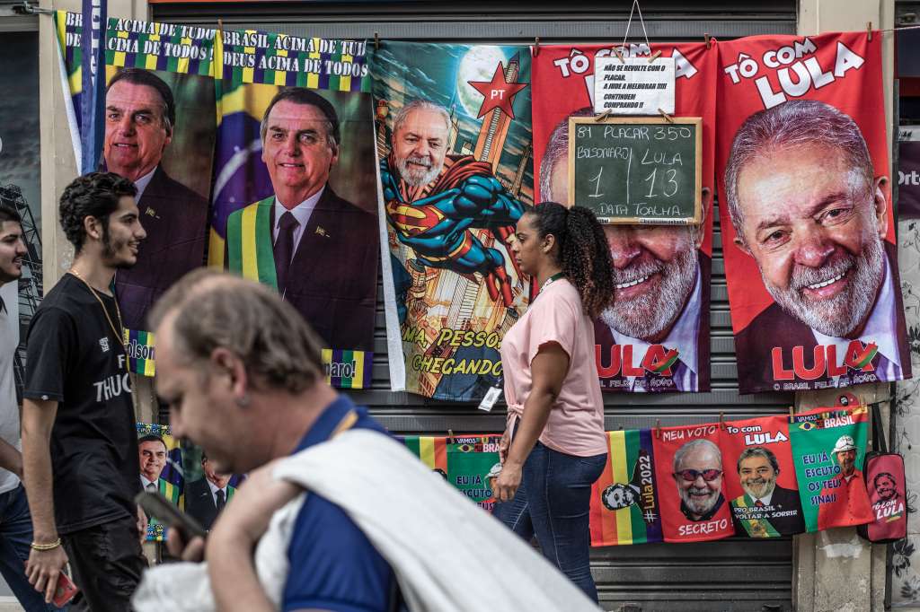 AME327. RÍO DE JANEIRO (BRASIL), 28/09/2022.- Varias personas caminan frente a un puesto callejero de toallas con imágenes del actual presidente de Brasil y candidato a la reelección, Jair Bolsonaro, y su contendiente, el expresidente brasileño Luiz Inácio Lula da Silva, el 27 de septiembre de 2022, en Río de Janeiro (Brasil). Los brasileños acudirán el próximo domingo a las urnas en unas elecciones envueltas en un inédito clima de tensión, alimentado por las dudas que ha sembrado el presidente Jair Bolsonaro acerca de si reconocerá la eventual derrota que le vaticinan todas las encuestas. EFE/ André Coelho