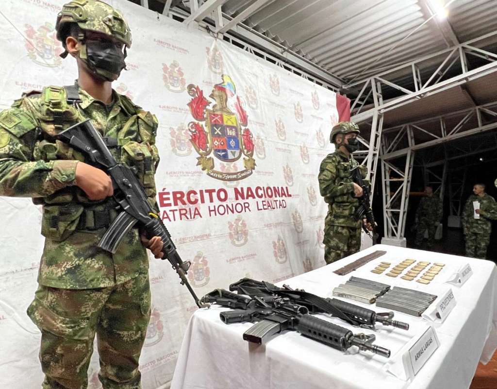 dos soldados con fusil, frente a una mesa con material de guerra incautado.