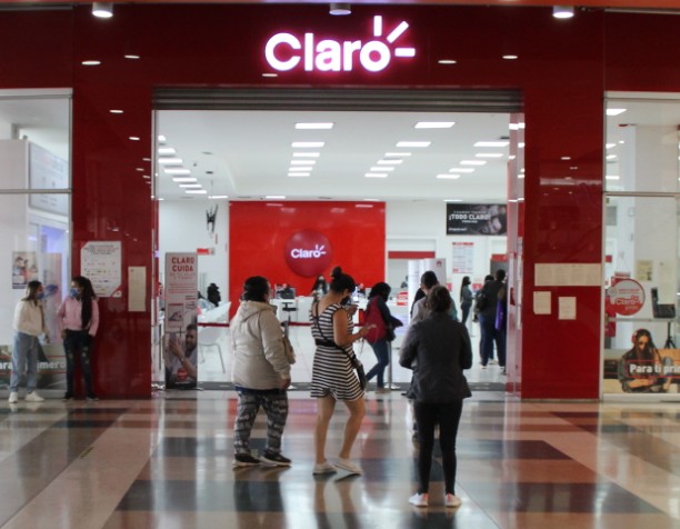 Varias personas caminan un un centro comercial. Al fondo se ve una sede del operador Claro.