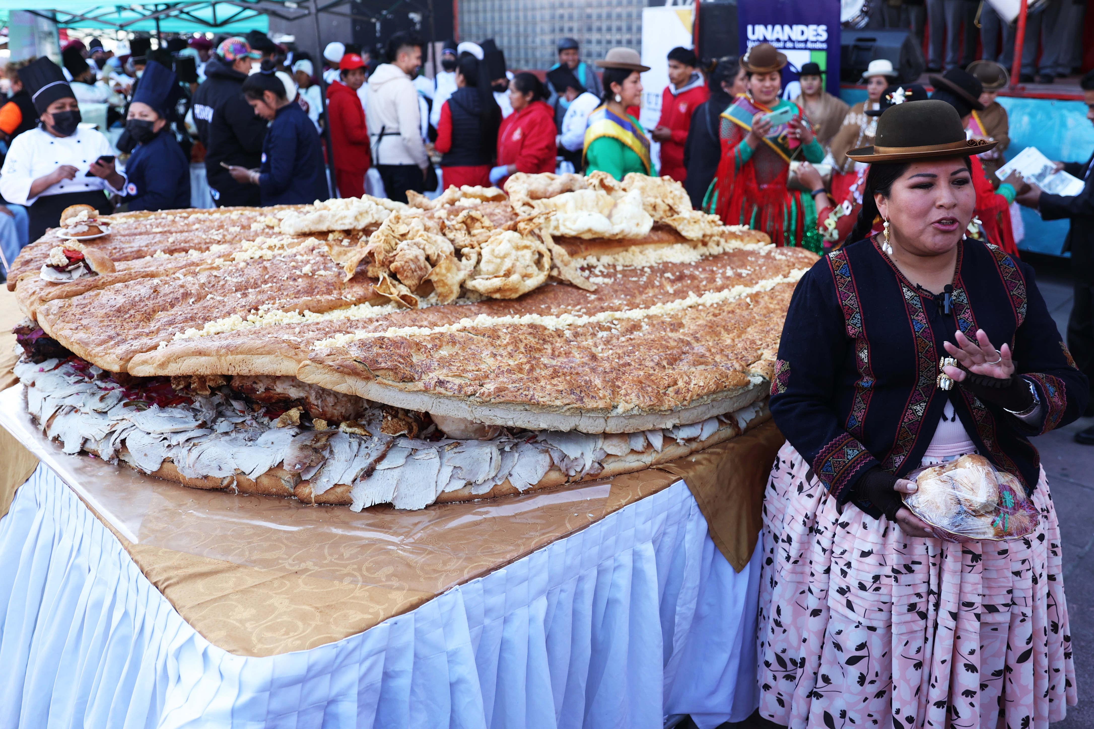 AME8792. LA PAZ (BOLIVIA), 02/07/2024.- Una mujer aimara posa junto al Sándwich de chola más grande del mundo, este martes en La Paz (Bolivia). Un centenar de cocineros de Bolivia prepararon durante dos días un sándwich de más de dos metros de diámetro, y lo presentaron este martes frente a decenas de bolivianos, en un evento para reivindicar la gastronomía de la ciudad de La Paz y sus ingredientes y la comida tradicional. EFE/ Luis Gandarillas