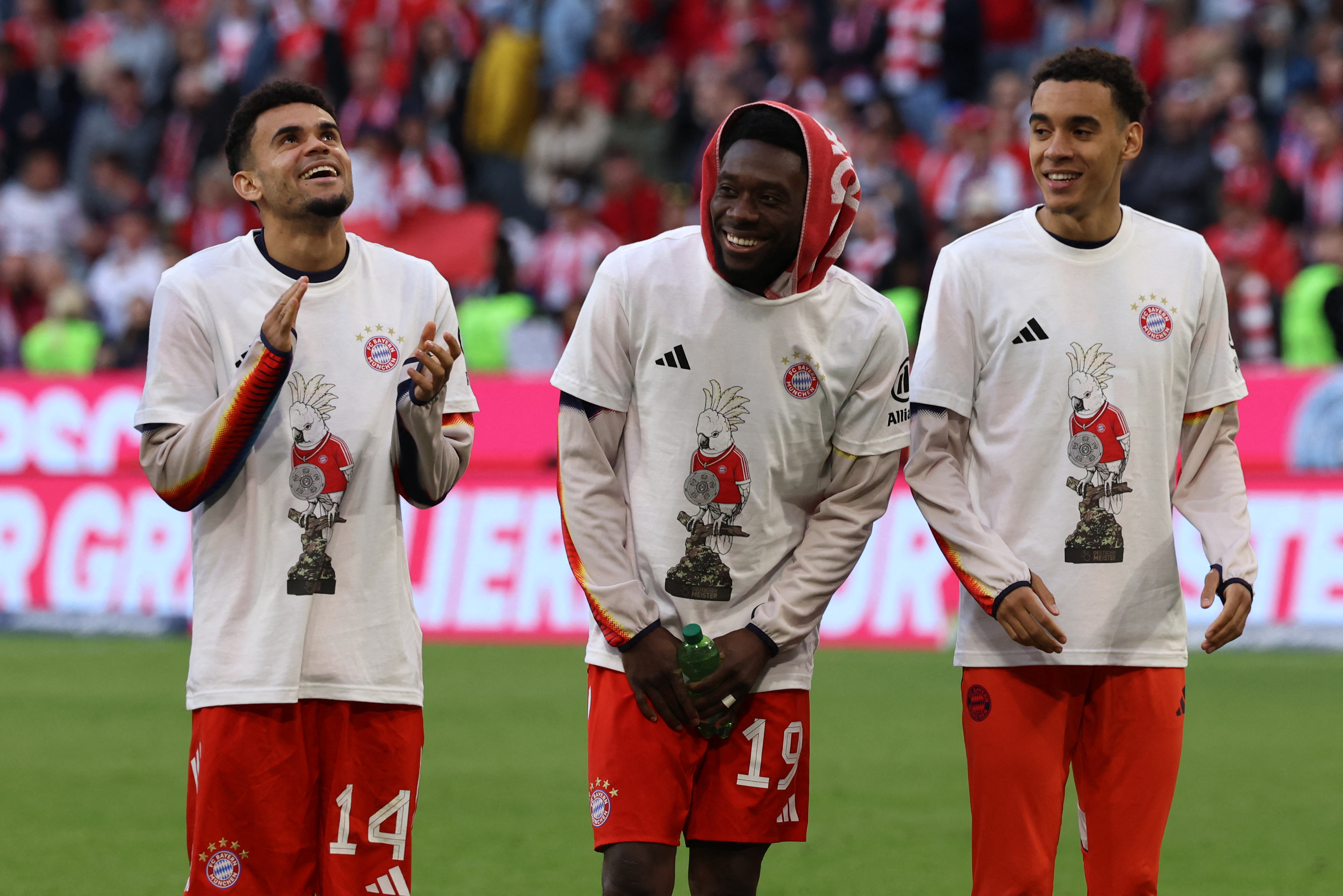Bayern Munich's Colombian forward #14 Luis Diaz, Bayern Munich's Canadian defender #19 Alphonso Davies and Bayern Munich's German midfielder #10 Jamal Musiala celebrate after winning the German first division Bundesliga football match between FC Bayern Munich and VfB Stuttgart in Munich, southern Germany, on April 19, 2026. Harry Kane scored his 32nd goal of the campaign as Bayern Munich cruised to a 4-2 home win over Stuttgart and claim a record-extending 35th Bundesliga title. (Photo by Alexandra BEIER / AFP) / DFL REGULATIONS PROHIBIT ANY USE OF PHOTOGRAPHS AS IMAGE SEQUENCES AND/OR QUASI-VIDEO