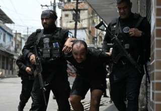 TOPSHOT - A suspect is escorted by police officers after being arrested during the Operacao Contencao (Operation Containment) at the Vila Cruzeiro favela, in the Penha complex, in Rio de Janeiro, Brazil, on October 28, 2025.