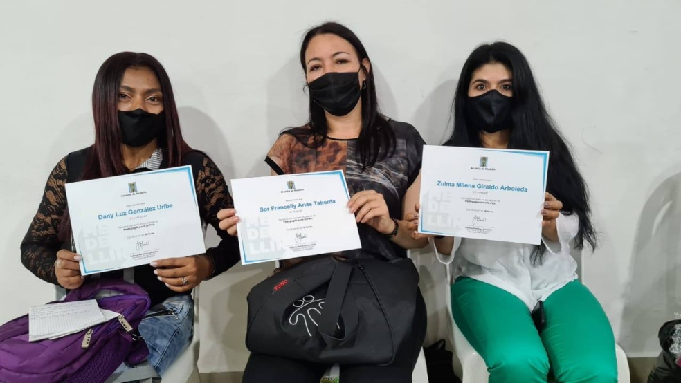 tres mujeres, con tapabocas, muestran sus diplomas de grado.