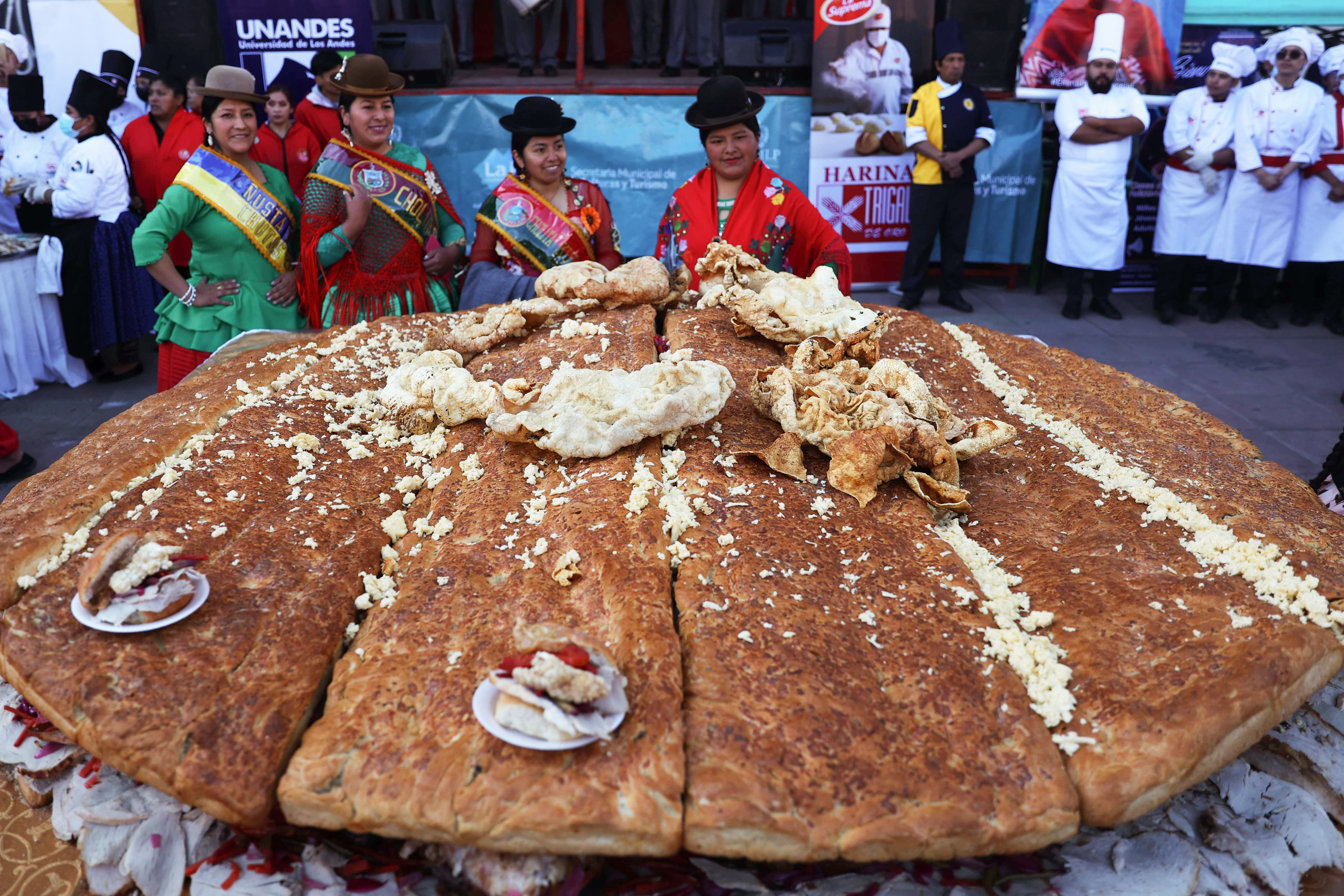 -FOTODELDÍA- AME8794. LA PAZ (BOLIVIA), 02/07/2024.- Mujer aimara posan junto al Sándwich de chola más grande del mundo, este martes en La Paz (Bolivia). Un centenar de cocineros de Bolivia prepararon durante dos días un sándwich de más de dos metros de diámetro, y lo presentaron este martes frente a decenas de bolivianos, en un evento para reivindicar la gastronomía de la ciudad de La Paz y sus ingredientes y la comida tradicional. EFE/ Luis Gandarillas