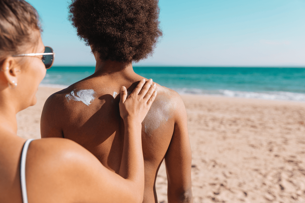 Una pareja en la playa aplicándose bloqueador solar.