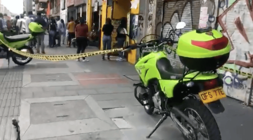 Varias personas detrás de una cinta de no pase. A la derecha una moto de la Policía