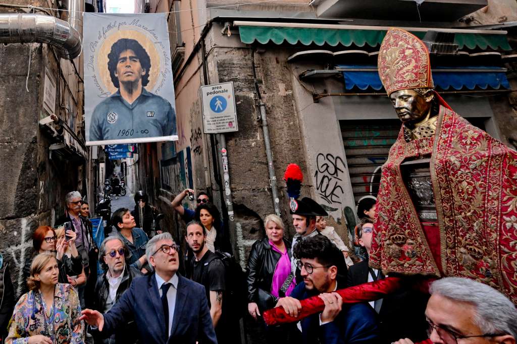 Naples (Italy), 06/05/2023.- People parade with a bust of San Gennaro near a photo of late soccer great Diego Maradona at the historic center of Naples, Italy, 06 May 2023. Faithful usually gather three times a year to witness the liquefaction of the otherwise coagulated blood of San Gennaro the patron saint of Naples. This year the procession was not only followed by the many faithful, who accompanied San Gennaro from the Duomo to the church of Santa Chiara, but also by the hundreds of tourists who flock to the capital of Campania. The parade took place under hundreds of blue flags and banners that have adorned the streets of Naples to celebrate after Napoli clinched their third-ever Serie A league title. (Italia, Nápoles) EFE/EPA/CIRO FUSCO