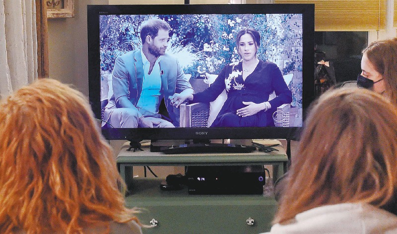 TOPSHOT - This photo illustration shows people wearing face masks, watch a televised conversation between Britain's Prince Harry with his wife Meghan Markle and US host Oprah Winfrey, in Arlington, Virginia March 7, 2021. Britain's royal family on Sunday braced for further revelations from Prince Harry and his American wife, Meghan, as a week of transatlantic claim and counter-claim reaches a climax with the broadcast of their interview with Oprah Winfrey. The two-hour interview with the US TV queen is the biggest royal tell-all since Harry's mother princess Diana detailed her crumbling marriage to his father Prince Charles in 1995. / AFP / OLIVIER DOULIERY