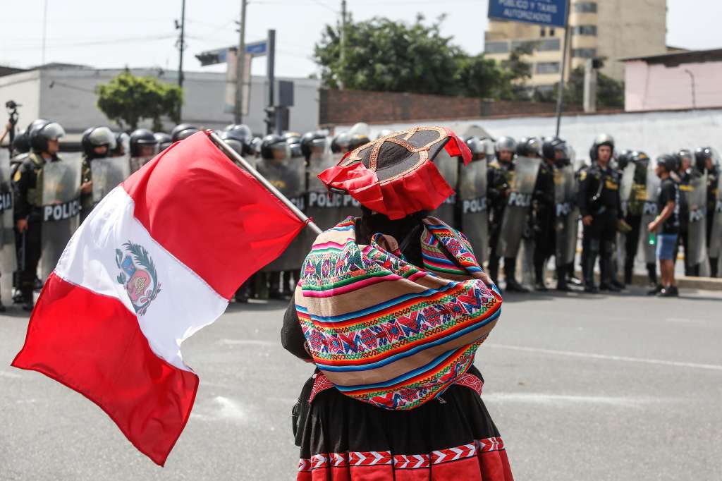 AME6110. LIMA (PERÚ), 28/07/2023.- Una mujer ondea una bandera frente a policías alineados hoy, en el centro de Lima (Perú). Los choques entre manifestantes y los agentes de seguridad se presentan en el mismo momento en el que la presidenta Dina Boluarte presenta ante el Congreso peruano su primer discurso con motivo del día de la Independencia. EFE/ Renato Pajuelo