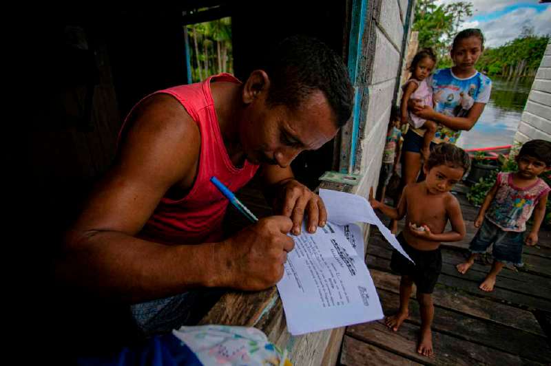 Un hombre firma un documento al recibir el kit escolar para sus hijos en el estado de Pará, Brasil. / AFP