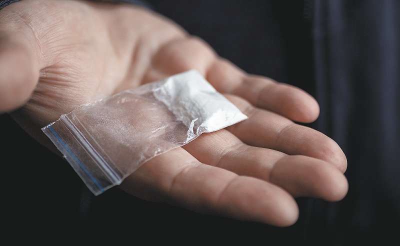 Mans hand holding on palm plastic packet with cocaine powder or another drugs. Drug dealer proposes to try narcotic concept, selective focus