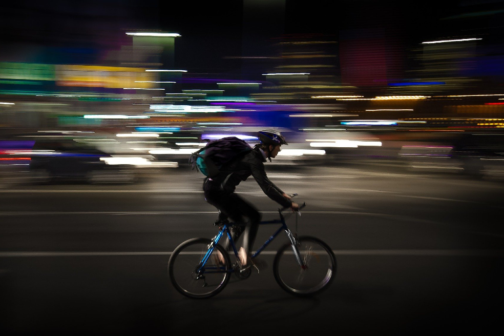 Un domiciliario en bicicleta se desplaza por una calle desconocida en la noche.
