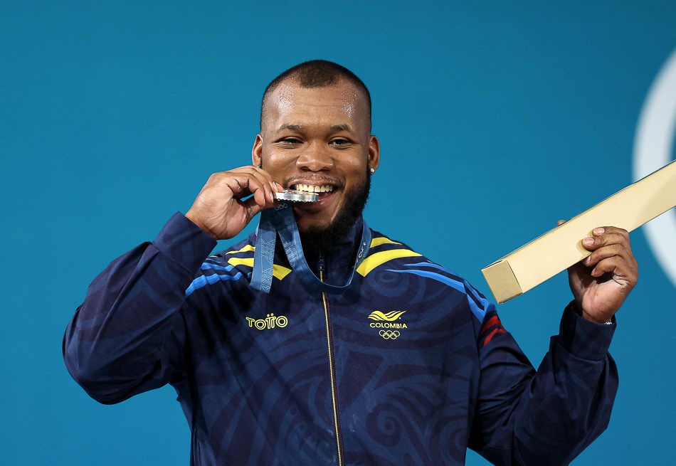 PARIS, FRANCE - AUGUST 09: Silver medallist Yeison Lopez of Team Colombia bites his medal on the podium during the Weightlifting Men's 89kg medal ceremony after the Weightlifting Men's 89kg on day fourteen of the Olympic Games Paris 2024 at South Paris Arena on August 09, 2024 in Paris, France. (Photo by Lars Baron/Getty Images)