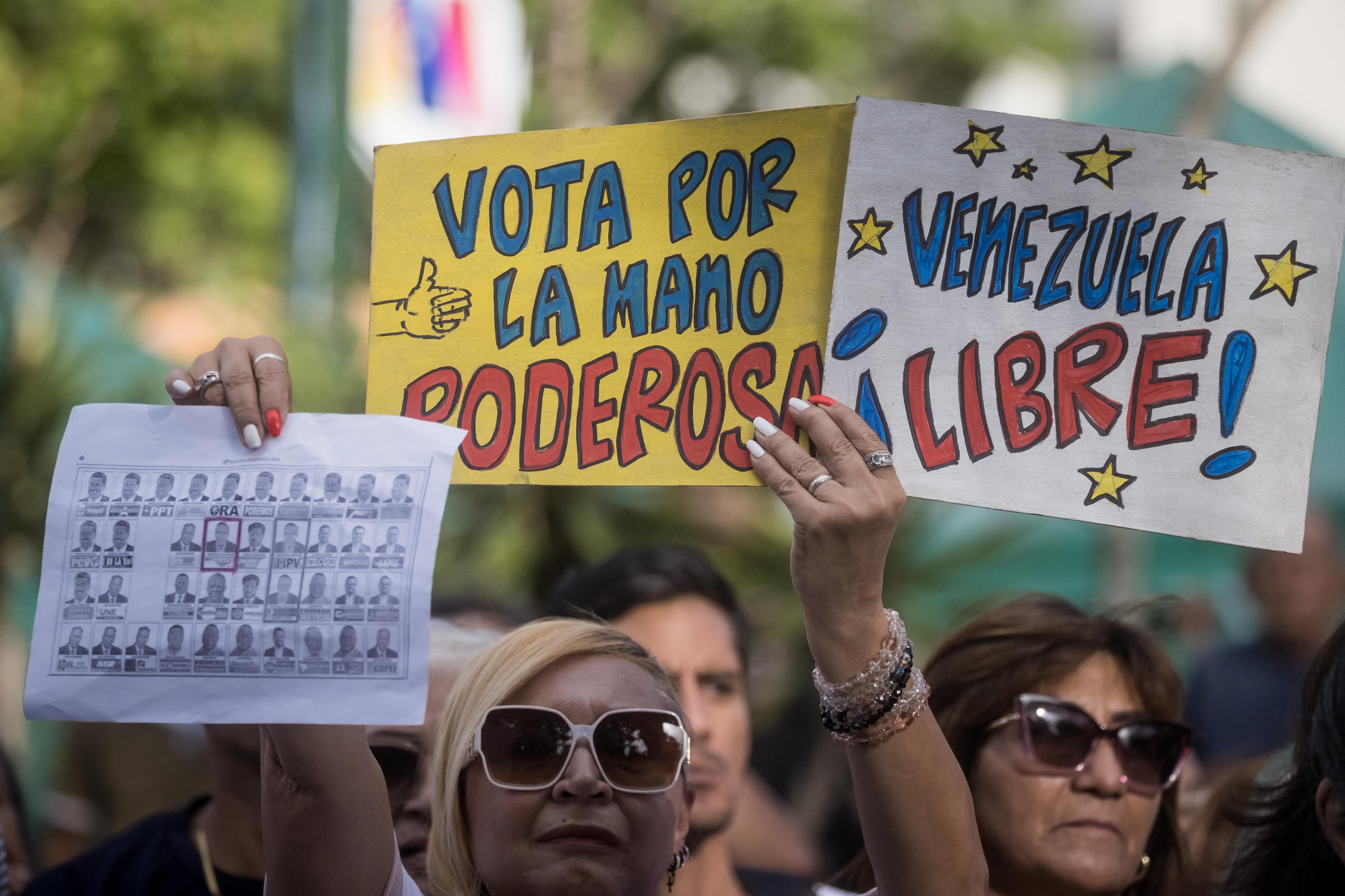 AME4078. CARACAS (VENEZUELA), 13/06/2024.- Una mujer muestra carteles en apoyo a Edmundo González Urrutia durante un acto político, este jueves en Caracas (Venezuela). González Urrutia, aseguró que, de ganar las elecciones presidenciales del próximo 28 de julio, trabajará por el "rescate" de las instituciones públicas de Venezuela, así como en una política económica que permita "salarios dignos" para los ciudadanos. EFE/ Miguel Gutierrez