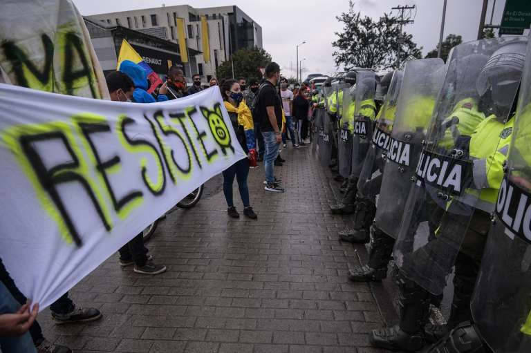 Varias personas sostienen un cartel que dice resiste frente de policías del Esmad