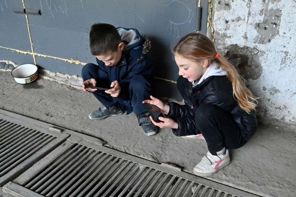 Un niño y una niña juegan con teléfonos inteligentes mientras se refugian de los bombardeos rusos en un estacionamiento subterráneo en Kharkiv, este de Ucrania.