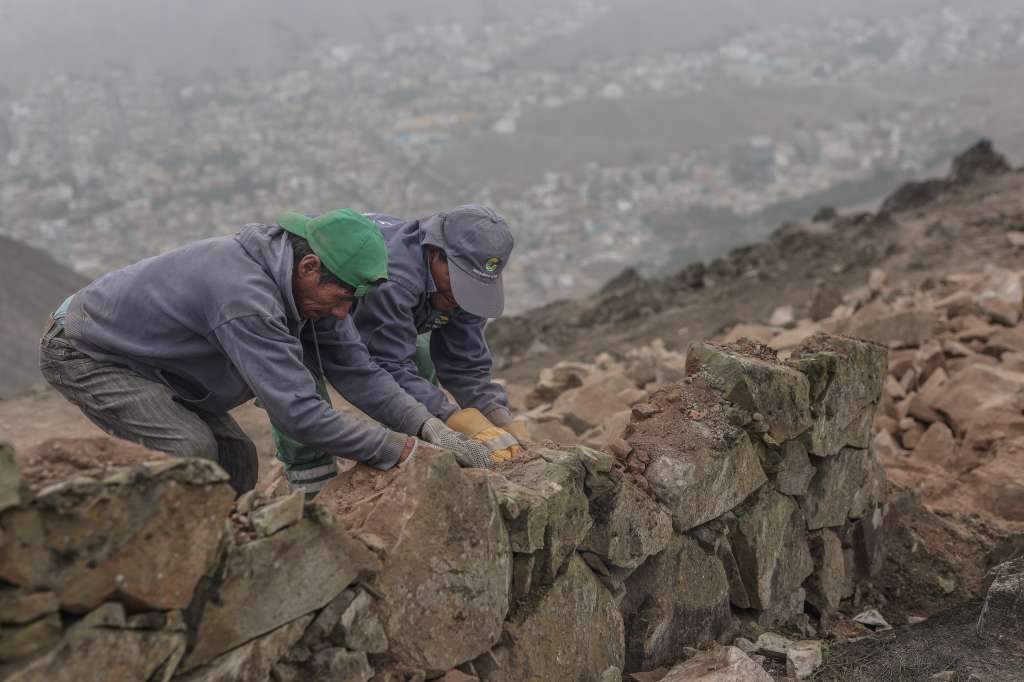 LIM01. LIMA (PERÚ), 05/09/2023.- Operarios trabajan en el desmonte de un muro que divide los distritos de La Molina y Villa del Triunfo hoy, en Lima (Perú). El denominado "muro de la vergüenza" de Lima, que separa a una humilde barriada de un distrito adinerado en la capital peruana, ha comenzado a ser demolido por orden del Tribunal Constitucional, una medida que ha suscitado comentarios de distinto signo a cada lado y que no cierra la brecha social abierta. El muro, en cuyo derribo trabajan operarios desde hace varios días, se ubica en lo alto de una loma que marca el límite entre el acomodado distrito de La Molina y el popular Villa del Triunfo, en pleno parque ecológico. EFE/ Aldair Mejía
