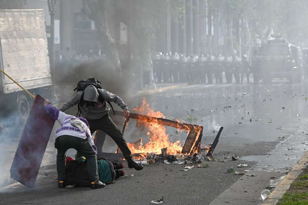 El fotoperiodista argentino Pablo Grillo (izq.) es retratado en el suelo, herido, durante una protesta de jubilados, apoyados por aficionados al fútbol, contra el gobierno del presidente Javier Milei en Buenos Aires