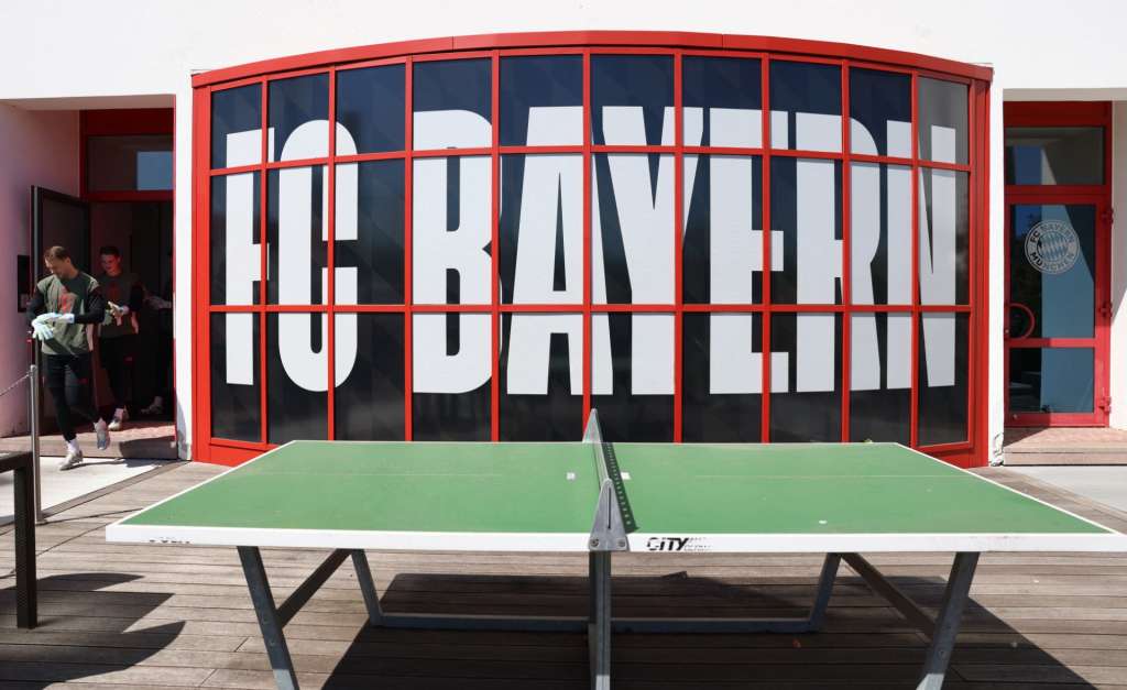 TOPSHOT - Bayern Munich's German goalkeeper #01 Manuel Neuer (L) and Bayern Munich's German goalkeeper #40 Jonas Urbig leave the sports cabin for a training session as the logo of FC Bayern Munich is seen at the training grounds behind a table tennis table in Munich, southern Germany on April 27, 2026, one day ahead of the UEFA Champions League semi-final first leg football match against Paris Saint-Germain (PSG) to be played in Paris. (Photo by Alexandra BEIER / AFP)