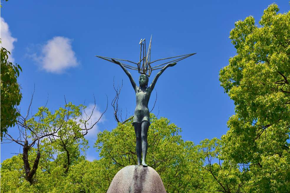 Estatua de Sadako Sasaki en el Parque de la Paz de Hiroshima. La foto fue tomada de día, el cielo está despejado y la estatua en honor a ella está en el centro de la imagen.