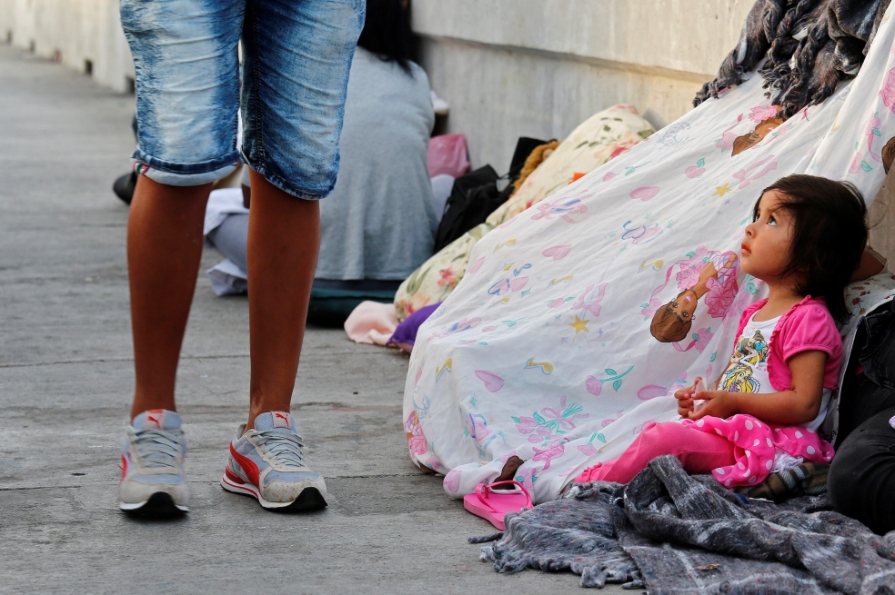 Una persona que se dirige a cruzar la frontera pasa delante de Jennifer, de 2 años, que aguarda junto a su madre Evelyn y otros solicitantes de asilo de Guatemala y Cuba en un puente para poder entrar en EE.UU. / EFE