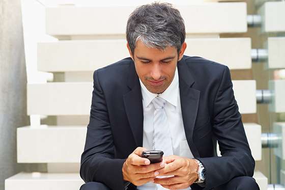 A handsome senior business man messaging while sitting on the stairs