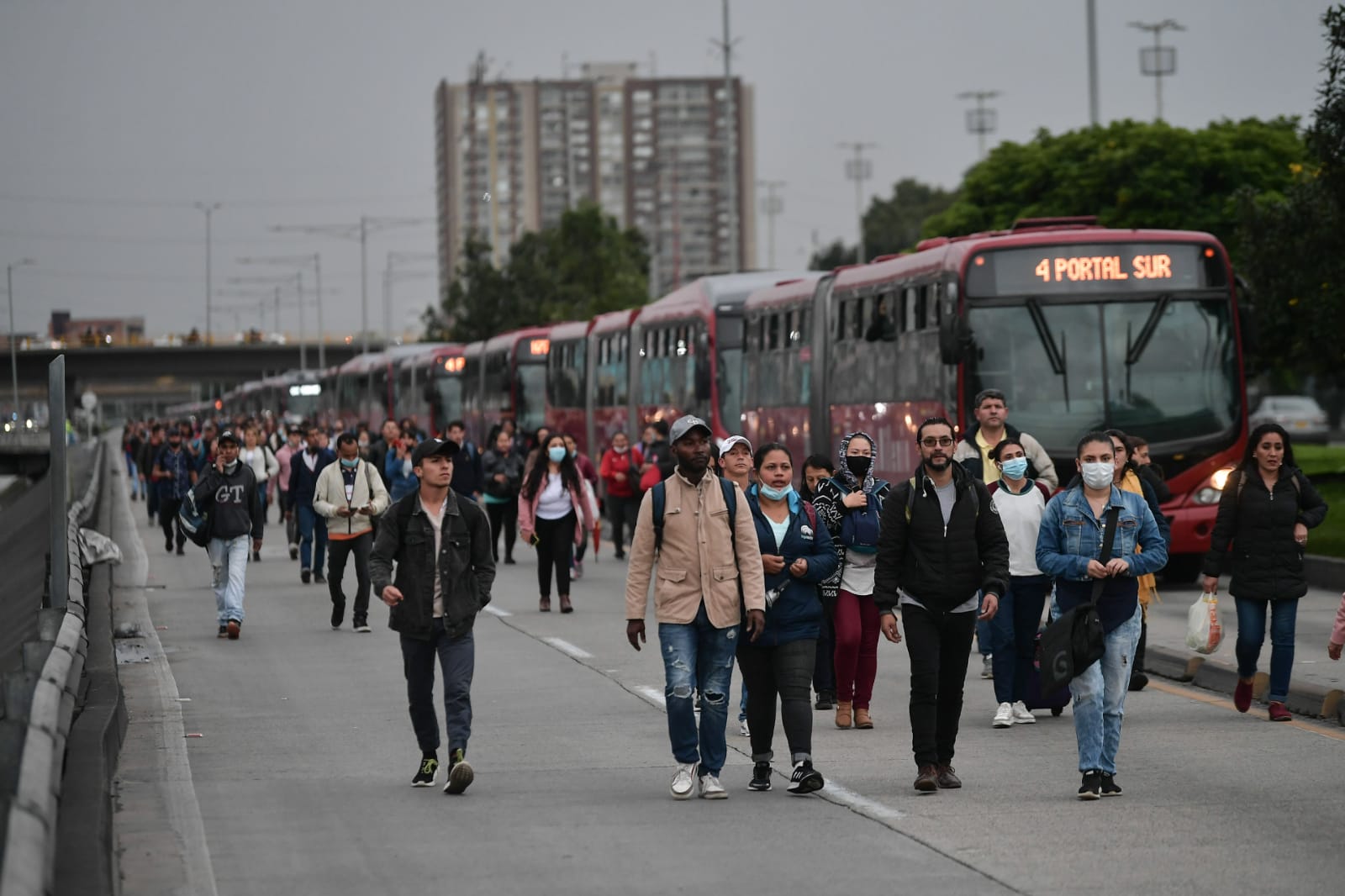 Filas de buses de Transmilenio detenidos junto a personas caminando a sus destinos.