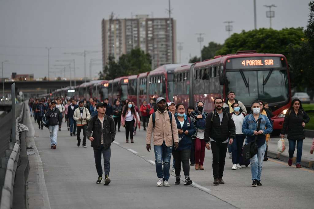 Filas de buses de Transmilenio detenidos junto a personas caminando a sus destinos.
