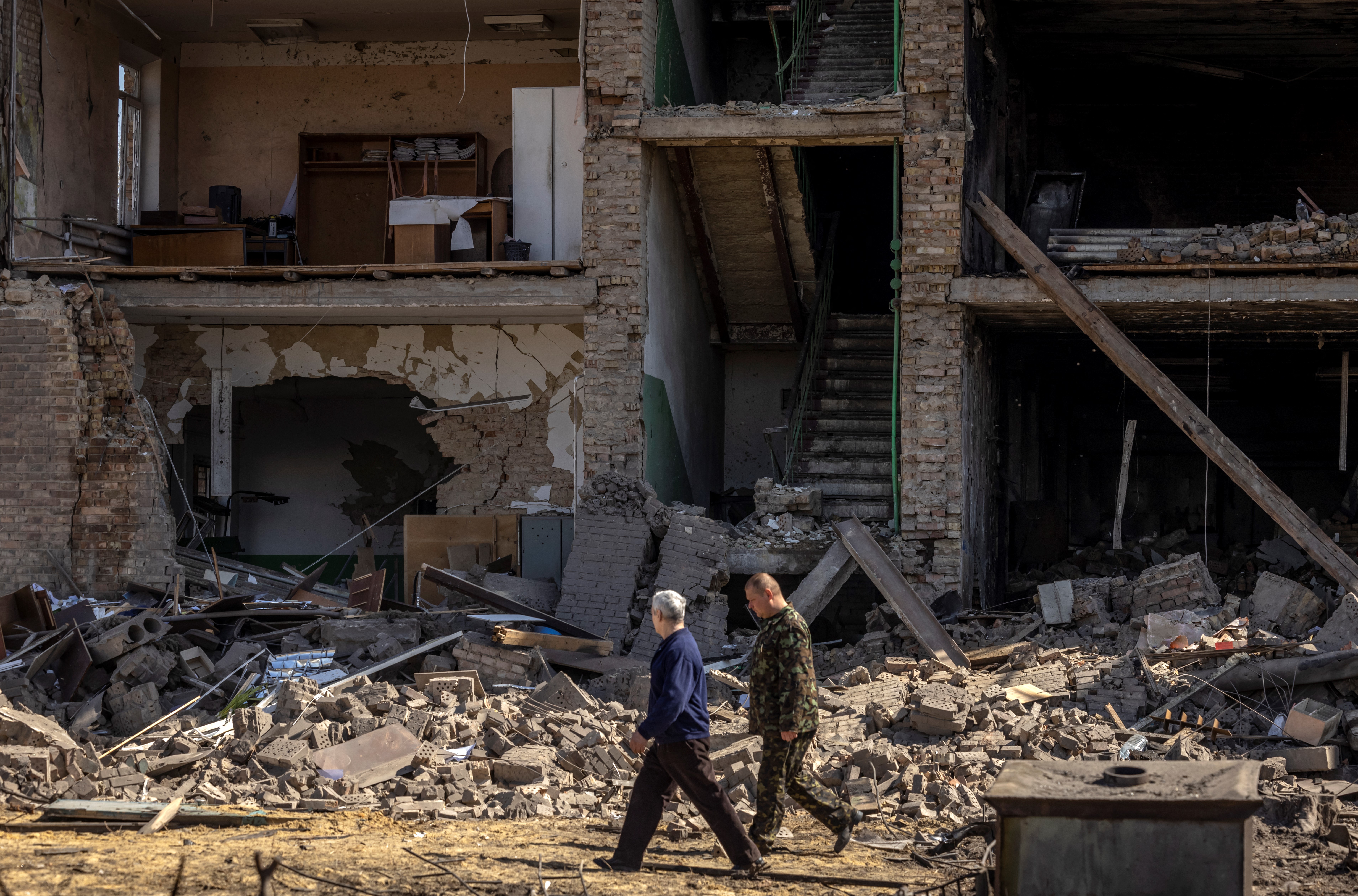 La gente pasa frente a un edificio con una fachada derrumbada en el complejo militar-industrial de la compañía Vizar, después de que el sitio fuera atacado durante la noche por ataques rusos, en la ciudad de Vyshneve, suburbios del suroeste de Kiev, el 15 de abril de 2022.
