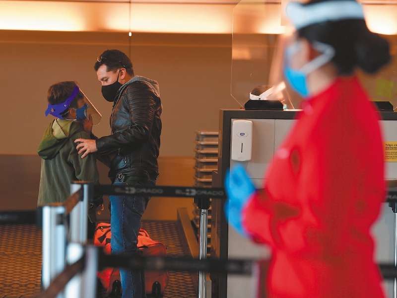 Adulto y niño con tapabocas y máscara en el control de seguridad del aeropuerto El Dorado.