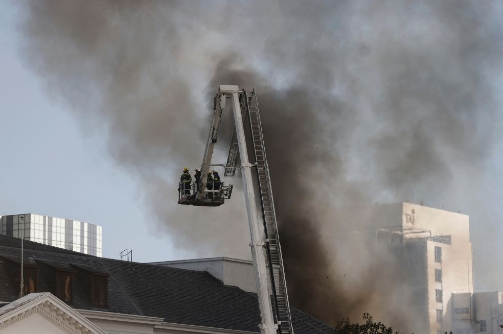 Los bomberos mueven una plataforma elevada de extinción de incendios cerca del techo del edificio de la Asamblea Nacional en Sudáfrica para tratar de apagar el fuego.