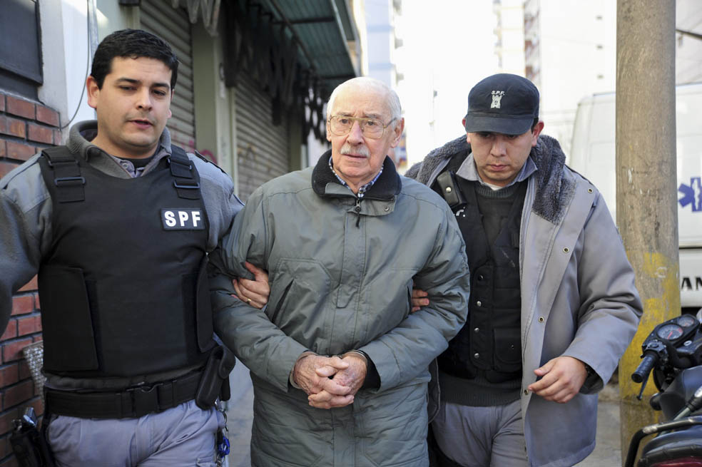 Jorge Rafael Videla en una fotografía captada en julio de 2012, mientras era escoltado por dos policías. / EFE