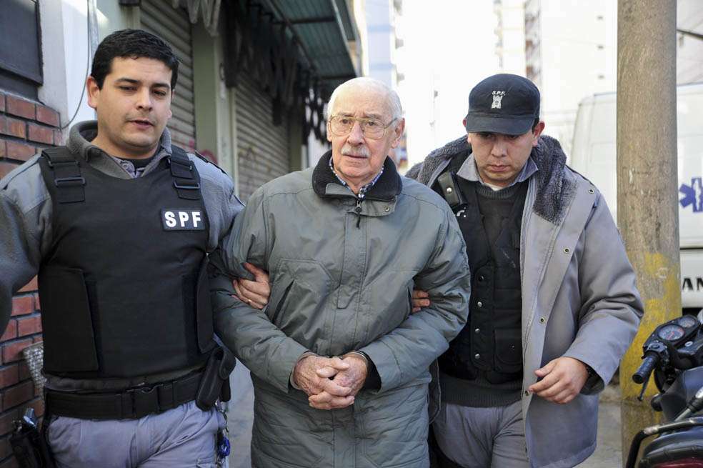 BUENOS AIRES (ARGENTINA). Fotografía de archivo del 17 de julio de 2012 en la que se observa al exdictador argentino Jorge Rafael Videla (c) escoltado por la policía en la localidad de San Martín, provincia de Buenos Aires (Argentina). Jorge Rafael Videla, condenado a prisión perpetua por delitos de lesa humanidad cometidos en el último régimen de facto (1976-1983), falleció el viernes 17 de mayo de 2013, en Buenos Aires a los 87 años, de muerte natural, confirmó el Servicio Penintenciario. Videla, quien estaba encarcelado en un penal de la provincia de Buenos Aires, fue el primer gobernante de la dictadura argentina condenado a prisión perpetua.