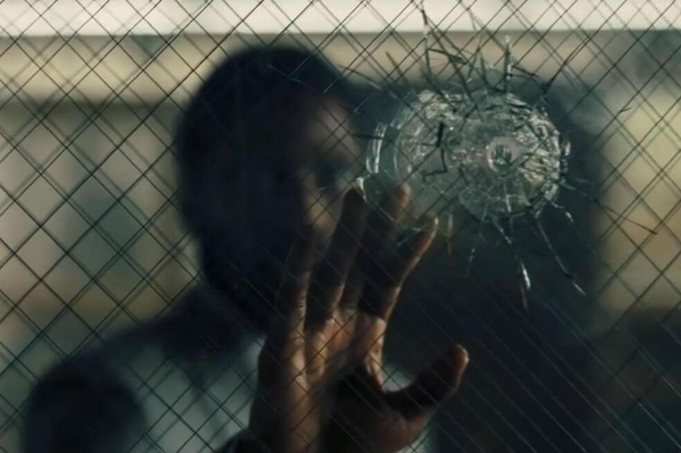 El adelanto muestra al protagonista de "Tenet", John David Washington, acercarse a un cristal para examinar unos impactos de bala. / Cortesía Warner Bros